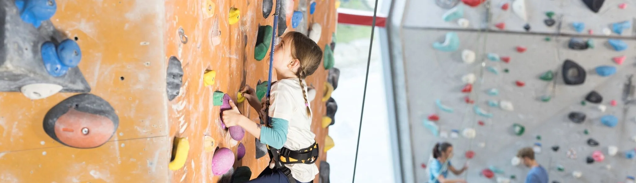 Ein Mädchen beim Familienklettern in der Kletterhalle des DAV. Im Hintergrund weitere Kletterer | © DAV / Jens Klatt